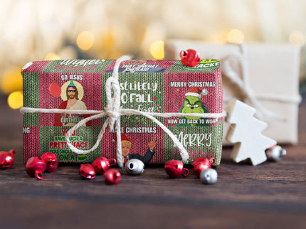 Ein kleines Geschenk, in lustigem Weihnachtspapier verpackt und mit weißer Schnur gebunden, steht auf einem Tisch. Um das Geschenk herum liegen rote und silberne Glöckchen, im Hintergrund ist eine unscharfe Lichterdekoration zu sehen.