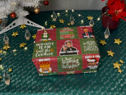 Eingepacktes Geschenk in humorvollem Meme-Weihnachtspapier, das Sprüche wie "Merry Christmas" und "Must Likely to Eat All the Cookies" zeigt. Im Hintergrund ein weißer Weihnachtsbaum, kleine Sterne und Mini-Bäume.
